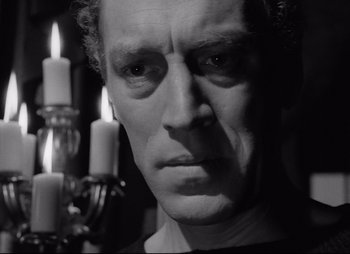 A black and white photo of a man with candles in the background