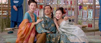 Movie still from “House of Flying Daggers” (2004), directed by Yimou Zhang – A man sitting between two women in traditional chinese clothing; Medium shot, Low angle