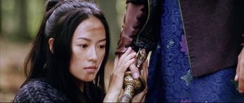 Movie still from “House of Flying Daggers” (2004), directed by Yimou Zhang – A woman holding a pair of boots while looking at the camera; Close Up shot, Over the shoulder angle