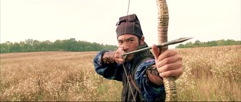 Movie still from “House of Flying Daggers” (2004), directed by Yimou Zhang – A man is holding a bow and arrow in a field; Medium shot, Over the shoulder angle