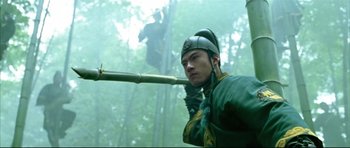 Movie still from “House of Flying Daggers” (2004), directed by Yimou Zhang – A man holding a bamboo stick while standing in the woods; Medium shot, Low angle