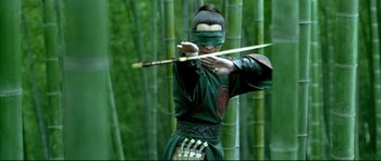 Movie still from “House of Flying Daggers” (2004), directed by Yimou Zhang – A man in a green outfit holding a wooden stick; Medium shot, Over the shoulder angle