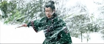 Movie still from “House of Flying Daggers” (2004), directed by Yimou Zhang – A man in a green coat is standing in the snow; Medium shot, Over the shoulder angle