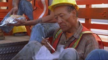 Movie still from “House of Sand and Fog” (2003), directed by Vadim Perelman – A man in a yellow hard hat is writing on a piece of paper; Medium shot, High angle