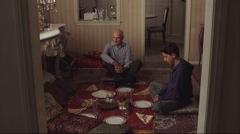 Movie still from “House of Sand and Fog” (2003), directed by Vadim Perelman – Two men sitting on the floor in front of a dinner table; Wide shot, High angle