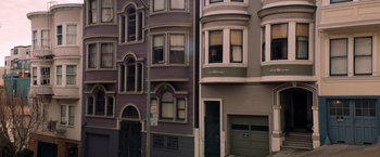 Movie still from “Venom” (2018), directed by Ruben Fleischer – A row of buildings in a city with a garage door open; Extreme Wide shot, High angle