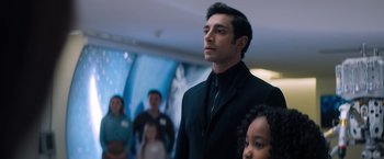 Movie still from “Venom” (2018), directed by Ruben Fleischer – A man in a suit and tie standing in front of a group of people; Medium shot, Over the shoulder angle