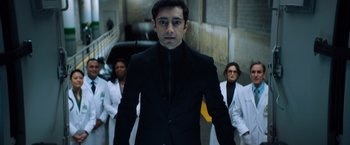 Movie still from “Venom” (2018), directed by Ruben Fleischer – A man in a black suit standing in front of two other people; Medium shot, Low angle