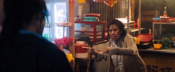 Movie still from “Venom” (2018), directed by Ruben Fleischer – An asian woman holding a walking stick in a store; Medium shot, Over the shoulder angle
