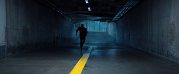 Movie still from “Venom” (2018), directed by Ruben Fleischer – A man is running through a tunnel with a yellow line; Wide shot, High angle