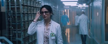 Movie still from “Venom” (2018), directed by Ruben Fleischer – A woman in a white lab coat and glasses in a hallway; Medium shot, Low angle