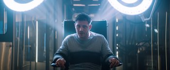 Movie still from “Venom” (2018), directed by Ruben Fleischer – A man sitting in a chair in a dark room; Medium shot, Low angle