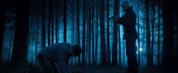 Movie still from “Venom” (2018), directed by Ruben Fleischer – Two people in the woods with one kneeling down and the other kneeling down; Wide shot, Low angle