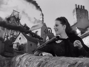 Movie still from “How Green Was My Valley” (1941), directed by John Ford – A young woman standing next to a wall with a factory in the background; Medium shot, Low angle