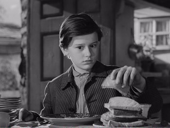Movie still from “How Green Was My Valley” (1941), directed by John Ford – A young man sitting at a table eating a sandwich; Medium shot, Over the shoulder angle