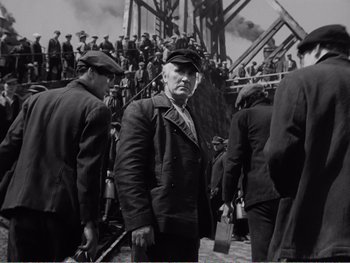 Movie still from “How Green Was My Valley” (1941), directed by John Ford – An older man in a hat and jacket standing in front of a group of people; Medium shot, Low angle