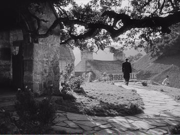 Movie still from “How Green Was My Valley” (1941), directed by John Ford – A man walking down a stone path under a large tree; Extreme Wide shot, Low angle