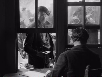 Movie still from “How Green Was My Valley” (1941), directed by John Ford – A man standing in front of a group of people looking out of a window; Medium shot, Over the shoulder angle