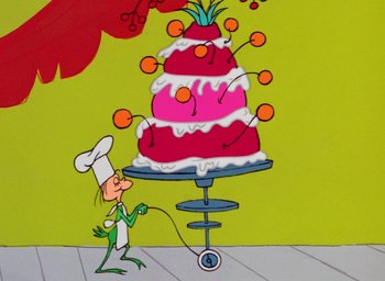 Movie still from “How the Grinch Stole Christmas!” (1966), directed by Ben Washam – A painting of a person holding an orange on top of a cake; Wide shot, High angle