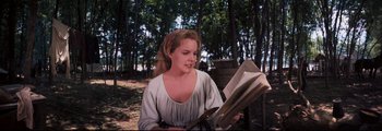 Movie still from “How the West Was Won” (1962), directed by George Marshall – A woman sitting in the woods reading a book; Medium shot, High angle