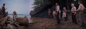 Movie still from “How the West Was Won” (1962), directed by George Marshall – A group of men standing on a beach next to water; Wide shot, Low angle
