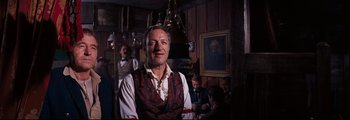 Movie still from “How the West Was Won” (1962), directed by George Marshall – An older man wearing a vest standing in front of a group of people; Medium shot, Low angle