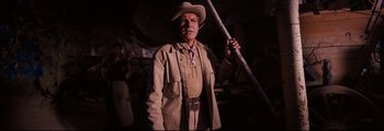Movie still from “How the West Was Won” (1962), directed by George Marshall – A man in a cowboy hat holding a wooden stick; Medium shot, Low angle