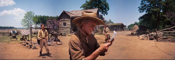 Movie still from “How the West Was Won” (1962), directed by George Marshall – A man in a cowboy hat is looking at a piece of paper; Medium shot, High angle