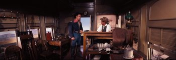Movie still from “How the West Was Won” (1962), directed by George Marshall – Two men are standing at a table talking; Wide shot, Over the shoulder angle
