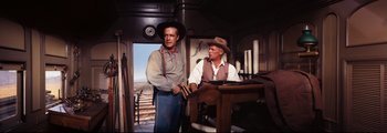 Movie still from “How the West Was Won” (1962), directed by George Marshall – A man and a man sitting at a table in a room; Medium shot, Over the shoulder angle