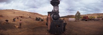 Movie still from “How the West Was Won” (1962), directed by George Marshall – A man standing in front of an old steam train; Wide shot, Low angle