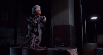 Movie still from “Howard the Duck” (1986), directed by Willard Huyck – A statue of a duck wearing a suit and tie; Wide shot, Low angle