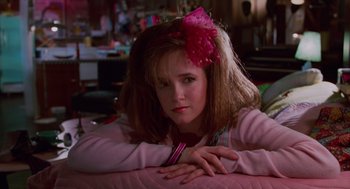 Movie still from “Howard the Duck” (1986), directed by Willard Huyck – A woman with a bow in her hair sitting on a bed; Close Up shot, Low angle