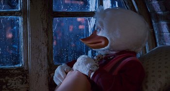 Movie still from “Howard the Duck” (1986), directed by Willard Huyck – A person wearing a duck mask looking out of a window; Close Up shot, Low angle
