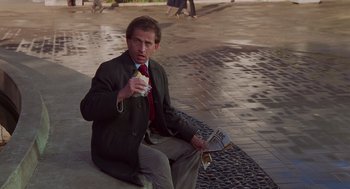 Movie still from “Howard the Duck” (1986), directed by Willard Huyck – A man sitting on the side of the street eating a sandwich; Medium shot, High angle