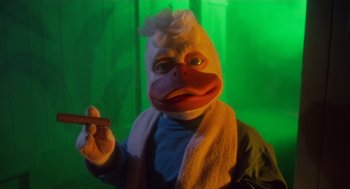 Movie still from “Howard the Duck” (1986), directed by Willard Huyck – A person in a duck costume holding a cigar; Medium shot, Low angle