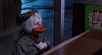 Movie still from “Howard the Duck” (1986), directed by Willard Huyck – A person wearing a duck mask sitting at a table; Medium shot, Low angle