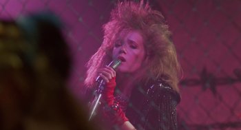 Movie still from “Howard the Duck” (1986), directed by Willard Huyck – A woman in a black jacket is holding a microphone; Close Up shot, Low angle