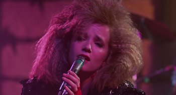 Movie still from “Howard the Duck” (1986), directed by Willard Huyck – A woman in a black jacket holding a microphone; Close Up shot, Low angle