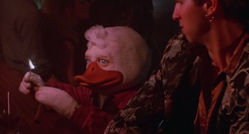 Movie still from “Howard the Duck” (1986), directed by Willard Huyck – A person wearing a duck mask in a room; Close Up shot, Over the shoulder angle
