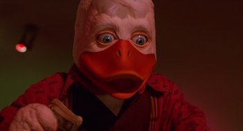 Movie still from “Howard the Duck” (1986), directed by Willard Huyck – A person wearing a duck mask and holding a knife; Close Up shot, Low angle