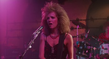 Movie still from “Howard the Duck” (1986), directed by Willard Huyck – A woman in a black top is playing a guitar; Close Up shot, Low angle