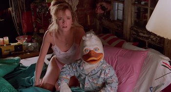 Movie still from “Howard the Duck” (1986), directed by Willard Huyck – A woman and a man dressed as a duck and a duck in pajamas; Medium shot, Low angle