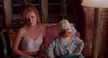 Movie still from “Howard the Duck” (1986), directed by Willard Huyck – A woman sitting next to a man wearing a duck mask; Medium shot, Low angle