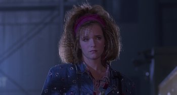 Movie still from “Howard the Duck” (1986), directed by Willard Huyck – A woman with a pink headband is standing in a dark room; Close Up shot, Low angle
