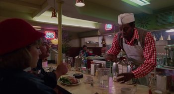Movie still from “Howard the Duck” (1986), directed by Willard Huyck – A man serving a plate of food at a restaurant; Medium shot, Over the shoulder angle