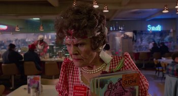 Movie still from “Howard the Duck” (1986), directed by Willard Huyck – An older woman in a red and white checkered shirt holding a book; Close Up shot, Low angle