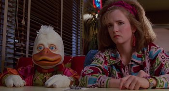 Movie still from “Howard the Duck” (1986), directed by Willard Huyck – A woman sitting at a table next to a stuffed duck doll; Close Up shot, Low angle