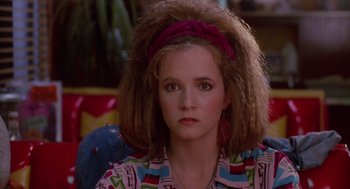 Movie still from “Howard the Duck” (1986), directed by Willard Huyck – A woman with a messy hair style sitting in a chair; Close Up shot, Over the shoulder angle