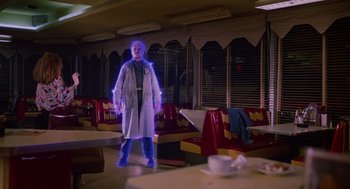 Movie still from “Howard the Duck” (1986), directed by Willard Huyck – A man in a lab coat standing next to a table; Wide shot, Low angle